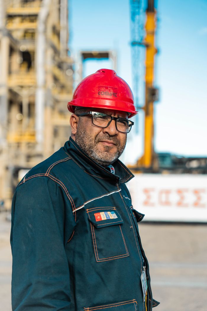 Portrait of a construction worker in red hard hat at an industrial site during daytime.